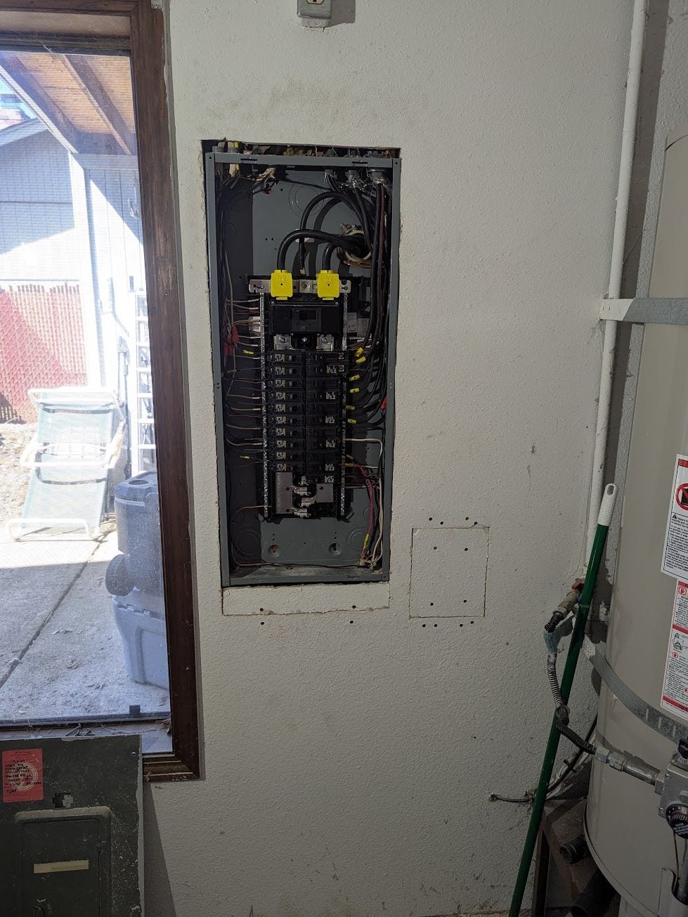 Electrical panel recessed into an exterior stucco wall beside a water heater
